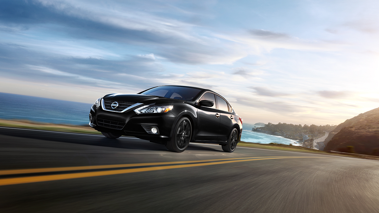 A 2017 Nissan Altima driving down a road next to an ocean