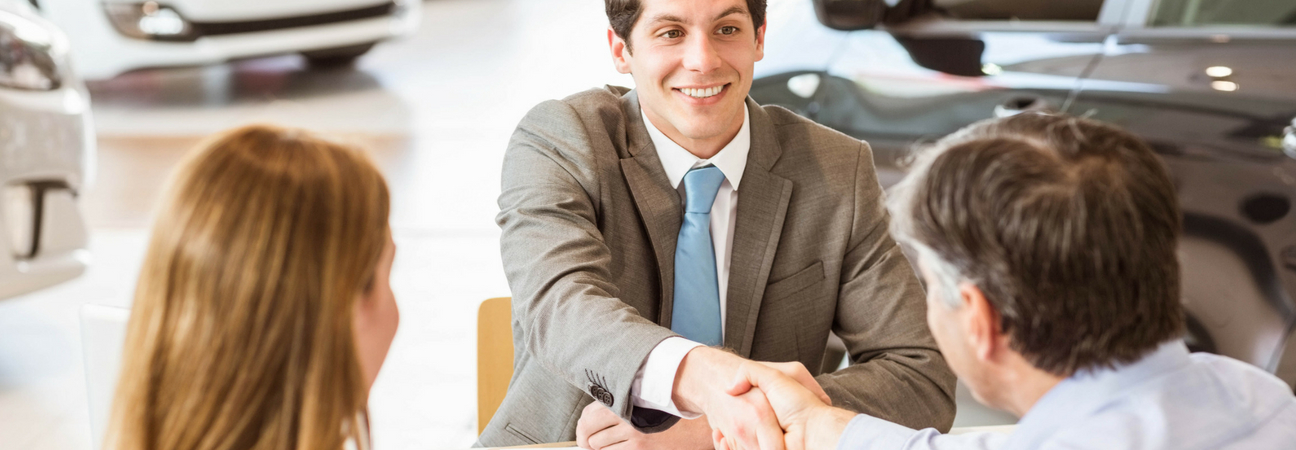 Customers shaking hands with young car salesman